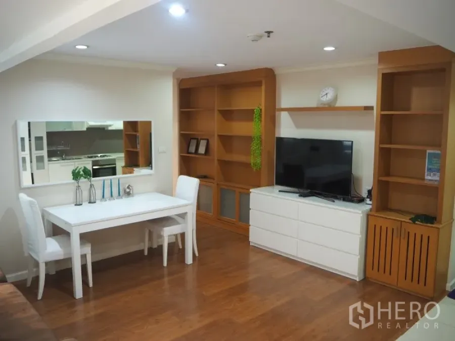 Condominium for rent or sale in Watthana, Bangkok - Bright living and dining area with white table, built-in wooden shelves, TV cabinet, and hardwood floors.