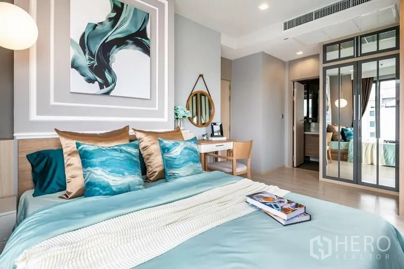 Condominium for rent or sale in Watthana, Bangkok - Primary bedroom with teal bedding, work desk, mirrored wardrobe and ensuite access.