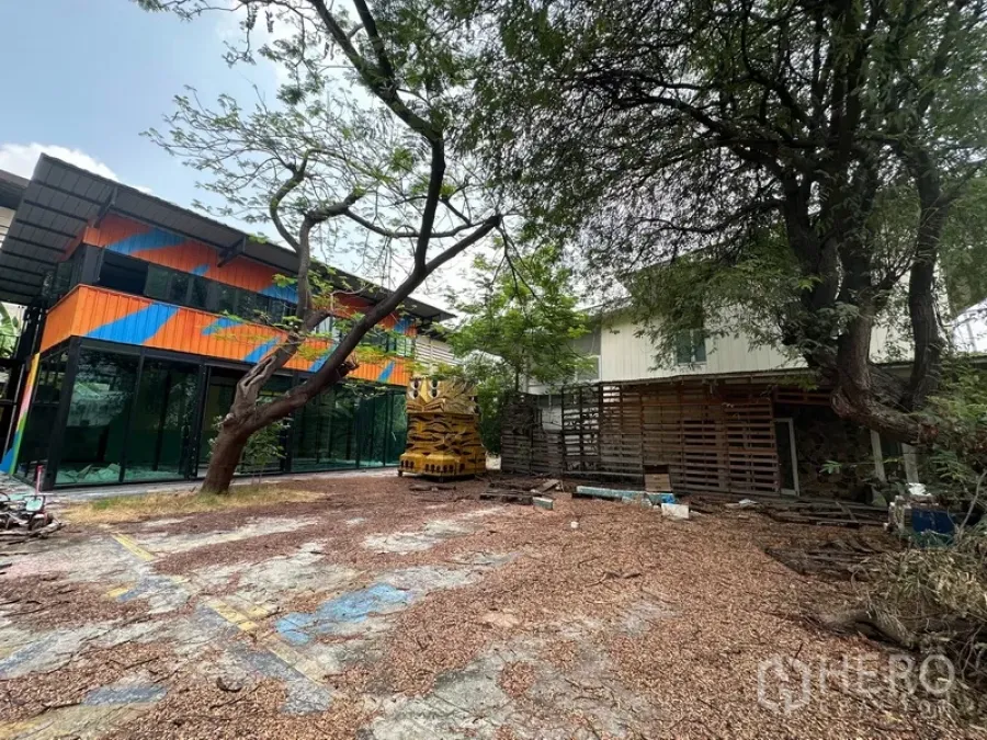 Detached House for rent in Watthana, Bangkok - Wide courtyard showing a colorful glass building and an older white house.