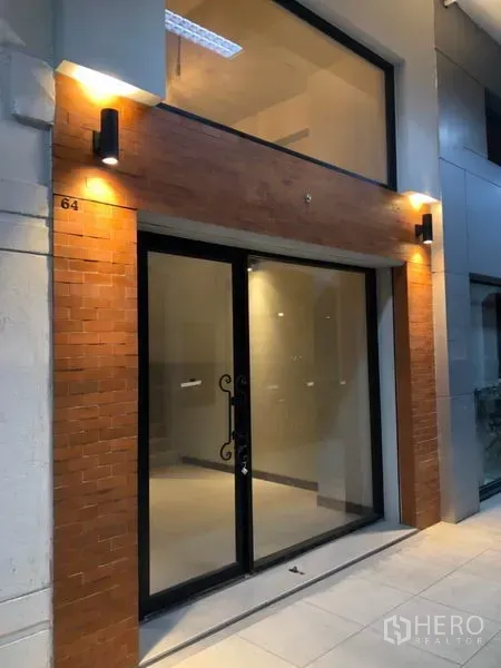 零售空间 出租在Watthana, Bangkok - 零售店面玻璃立面，砖饰面与挑高窗，夜间照明明亮。