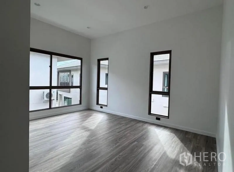 Detached House for rent in Bang Kapi, Bangkok - Bright corner bedroom upstairs with multiple windows and wood flooring.