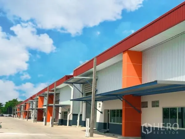 工厂 出租在Bang Phli, Samut Prakan - 现代厂房/仓库排屋，橙色外立面，带雨棚卸货口与宽阔车道，蓝天下景观