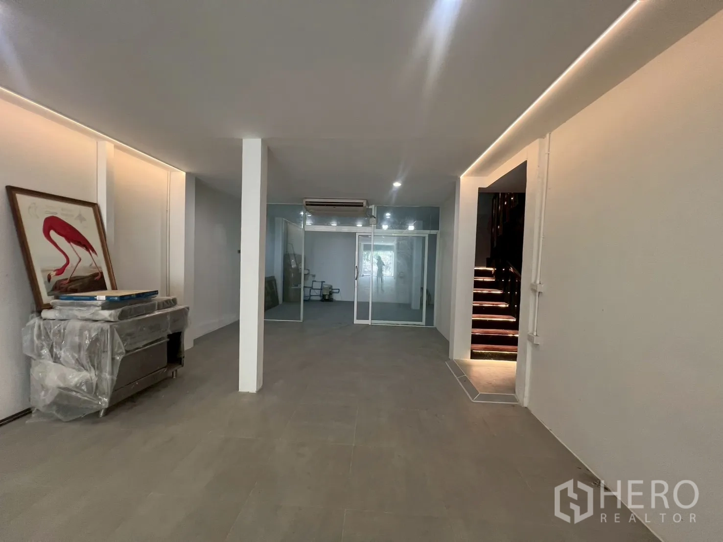 Home Office for rent in Watthana, Bangkok - Open workspace with a glass-partitioned room at the back and a lit wooden staircase.