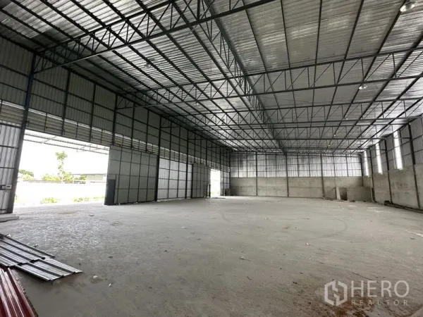 Warehouse for rent in Lam Luk Ka, Pathum Thani - Empty warehouse interior with high steel truss roof, skylight panels and reinforced concrete floor.