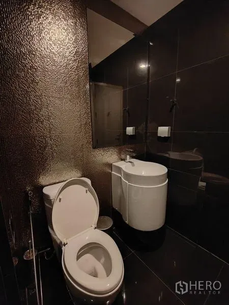 公寓 出租在Khlong Toei, Bangkok - 现代化浴室，深色瓷砖、马桶与圆角洗手台。
