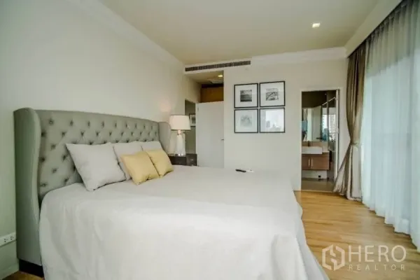 Condominium for rent or sale in Watthana, Bangkok - Master bedroom with upholstered headboard, large window, and access to an ensuite bathroom.