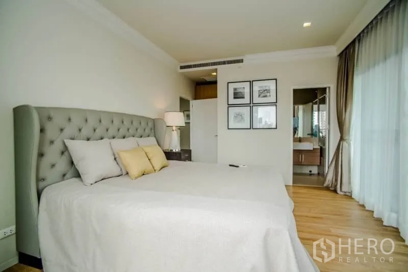 Condominium for rent or sale in Watthana, Bangkok - Master bedroom with upholstered headboard, large window, and access to an ensuite bathroom.