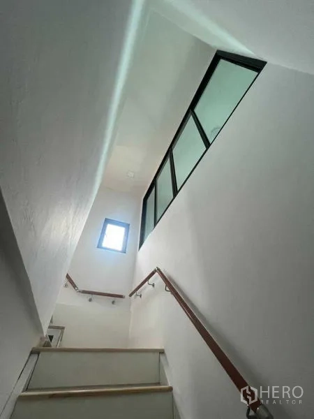 Home Office for sale - Stairwell between floors with window lighting and wooden handrails.
