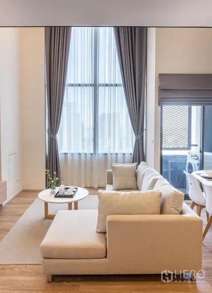 คอนโด ให้เช่าในKhlong Toei, Bangkok - โซฟา L‑shape รับแสงจากหน้าต่างสูงจรดเพดานพร้อมผ้าม่านโปร่ง
