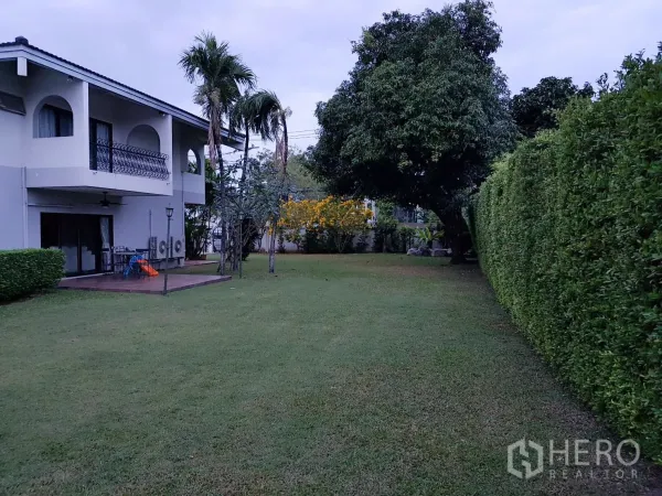 บ้าน ให้เช่าในKhan Na Yao, Bangkok - สวนส่วนตัวสนามหญ้าโล่ง รั้วไม้พุ่มสูง และระเบียงของบ้านสองชั้น