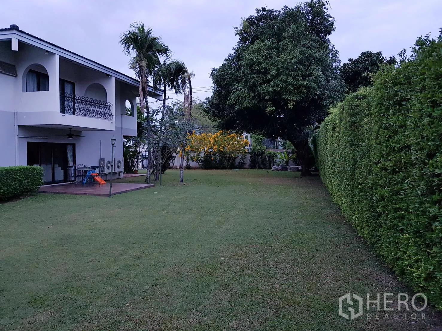 บ้าน ให้เช่าในKhan Na Yao, Bangkok - สวนส่วนตัวสนามหญ้าโล่ง รั้วไม้พุ่มสูง และระเบียงของบ้านสองชั้น