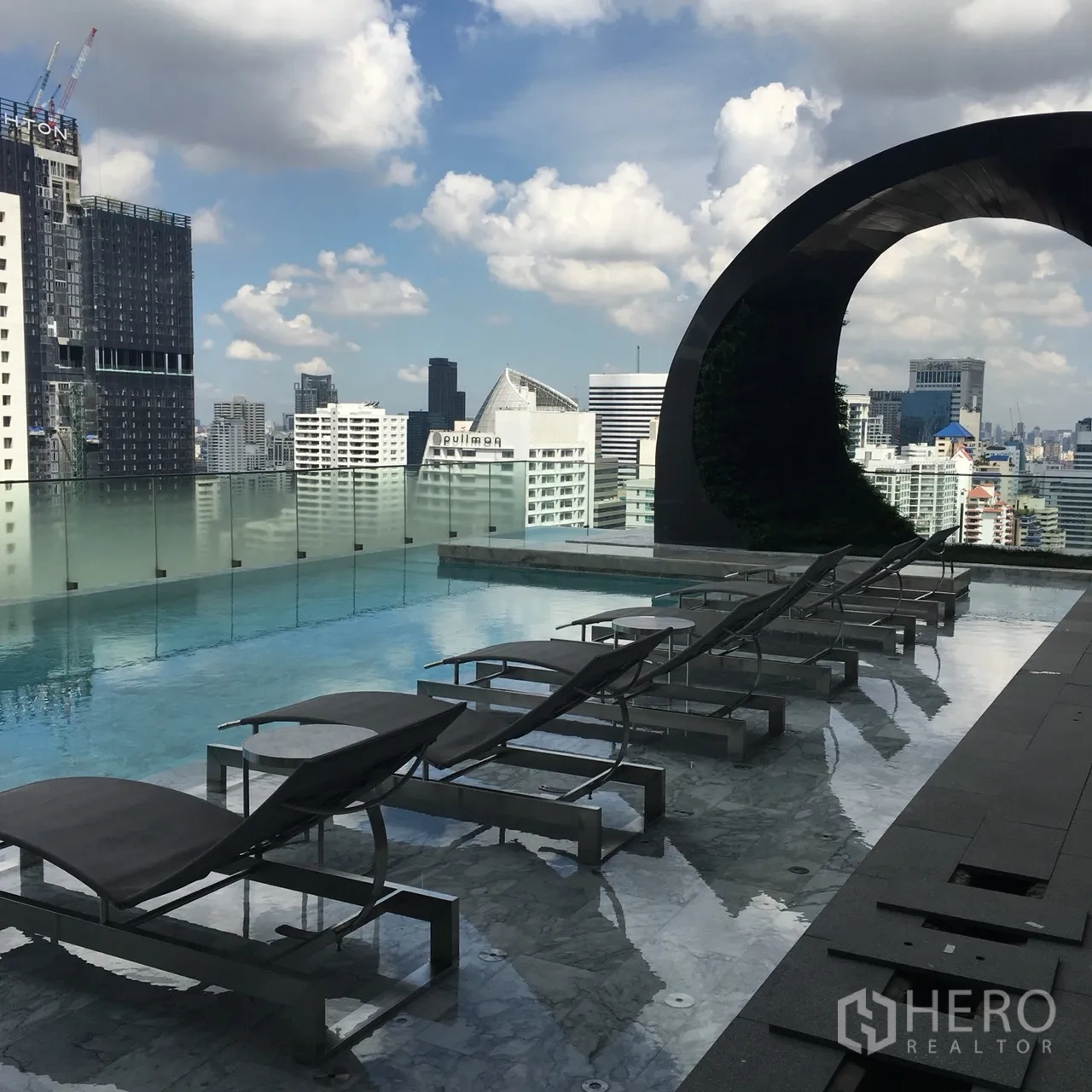 Condominium for rent or sale in Watthana, Bangkok - Rooftop infinity pool with sun loungers and Bangkok skyline views behind a glass railing.