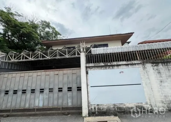Detached House for rent in Khlong Toei, Bangkok - Street-side view of the detached house behind a high wall and sliding gate.