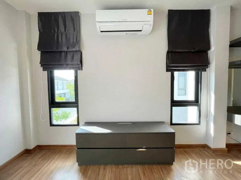 Detached House for rent in Don Mueang, Bangkok - Wall with split-type air conditioner between two windows and a low storage cabinet.