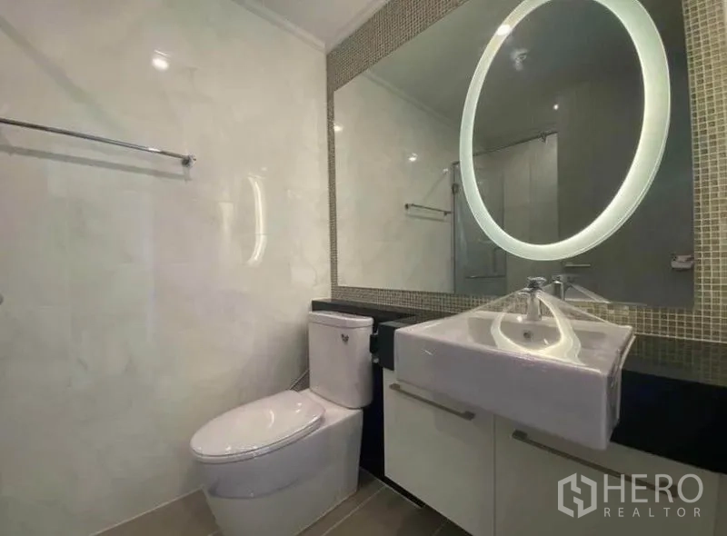 Condominium for rent in Watthana, Bangkok - Modern bathroom with illuminated round mirror, vanity, toilet and glass shower.