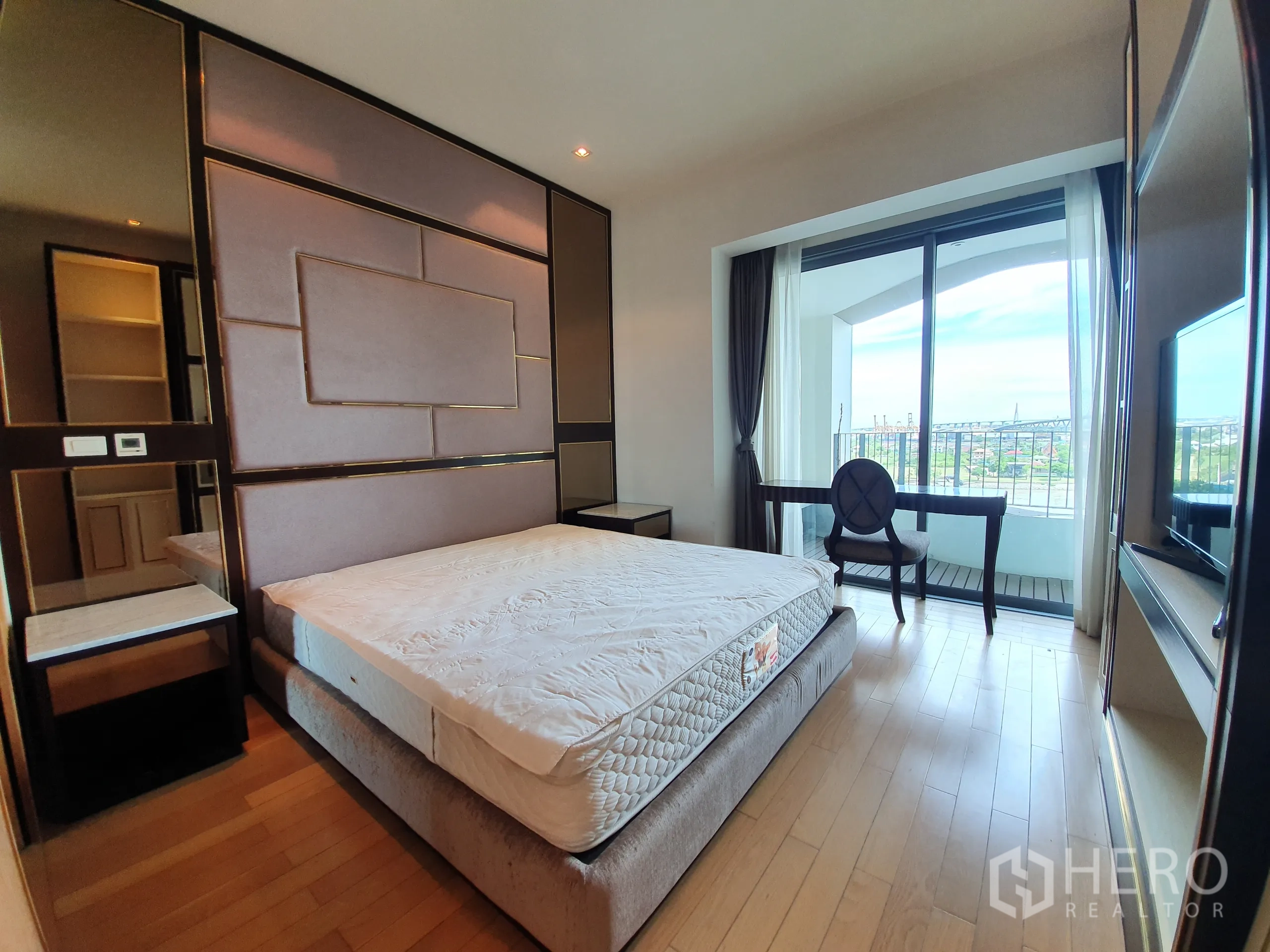 Condominium for rent or sale in Yan Nawa, Bangkok - Bedroom with upholstered feature wall, desk, and balcony doors opening to a river view.