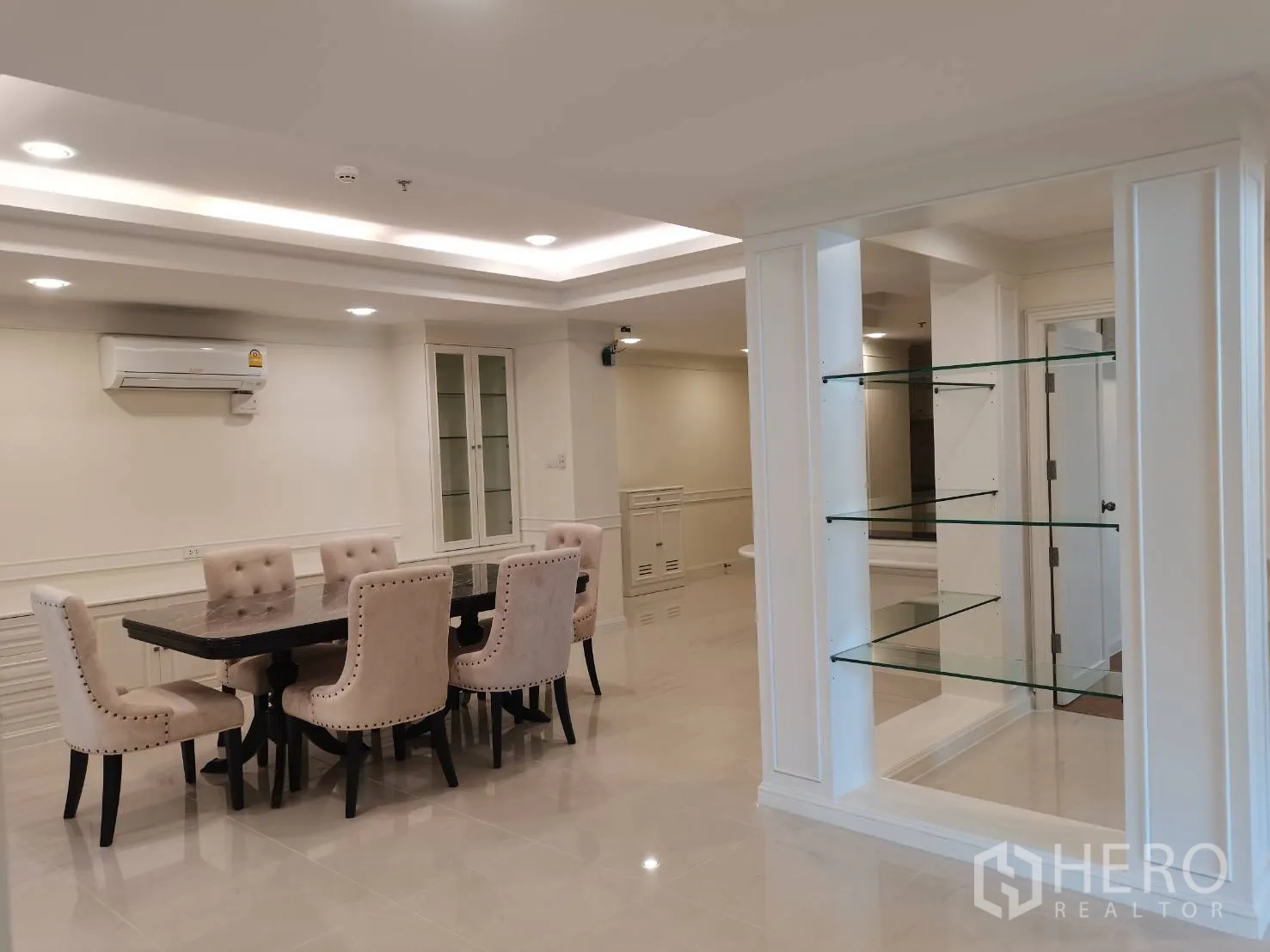 Condominium for rent in Watthana, Bangkok - Dining zone beside glass shelving and long built-in storage, air-conditioning mounted on wall.