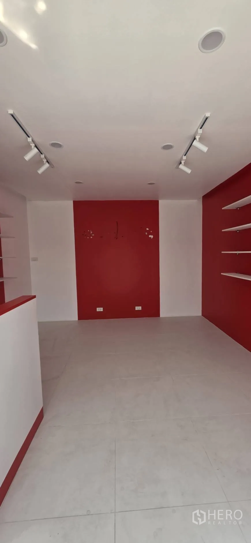 Retail Space for rent in Watthana, Bangkok - Front-to-back view of the shop highlighting tiled floors, red back wall, and ceiling spotlights.