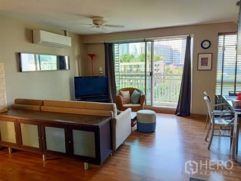 คอนโด ให้เช่าในKhlong Toei, Bangkok - ห้องนั่งเล่นเปิดโล่งพร้อมโซฟา ทีวี และประตูกระจกบานเลื่อนออกสู่ระเบียงวิวต้นไม้