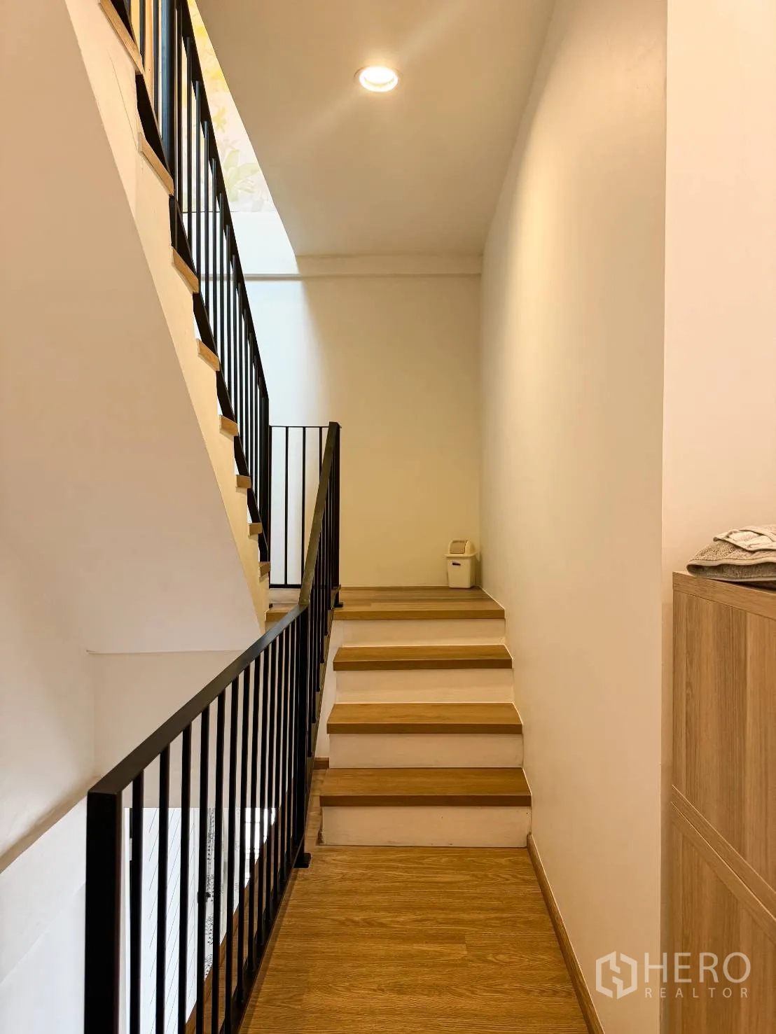 Shophouse for sale in Watthana, Bangkok - Interior staircase with black metal railing and wood steps under a skylight.