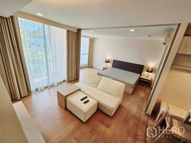Condominium for rent - Corner room with two tall windows, sofa and bed on wood flooring.
