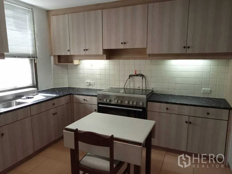 Condominium for rent in Watthana, Bangkok - Enclosed kitchen with light wood cabinets, oven and white tile backsplash.