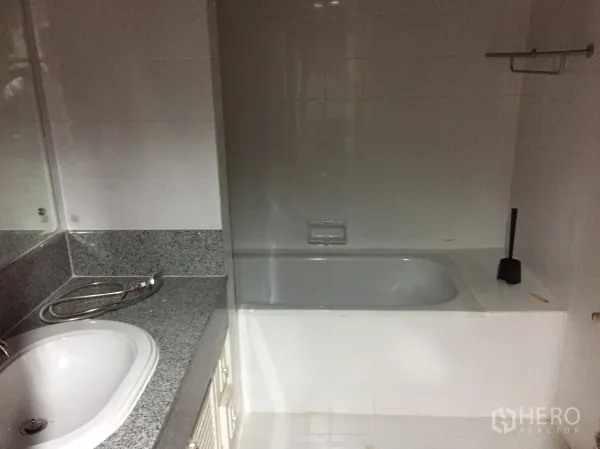 Condominium for rent in Watthana, Bangkok - Bathroom featuring a built-in bathtub, granite vanity countertop, large mirror, and white tiled walls.