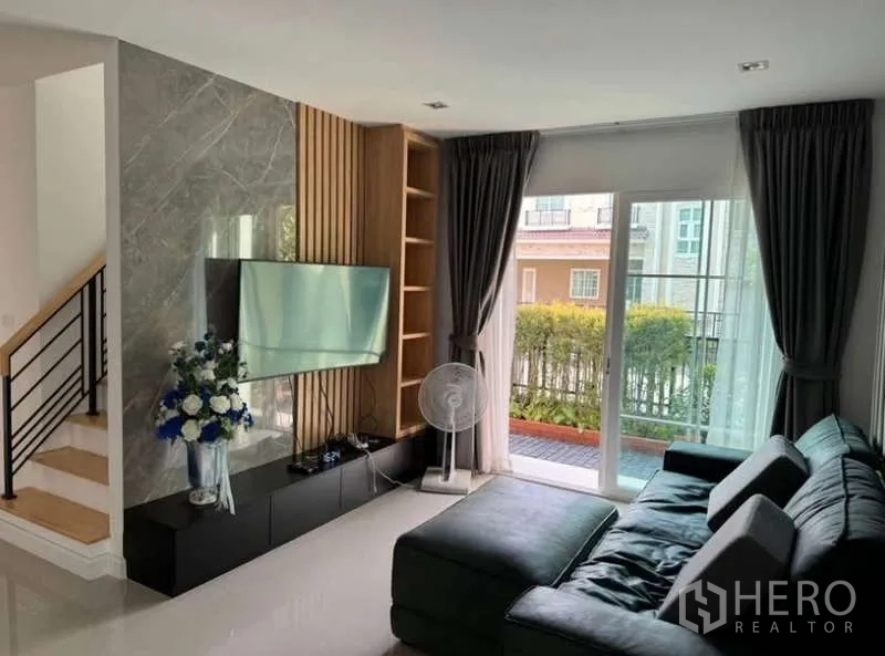 Detached House for rent in Bueng Kum, Bangkok - Living room with L-shaped sofa, TV feature wall and sliding glass doors to the patio.