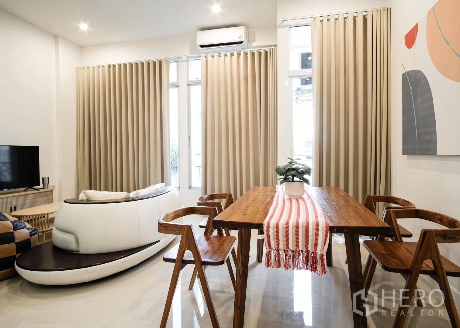 Townhouse for rent in Bang Phli, Samut Prakan - Open-plan dining and living space with wooden table, TV console, and floor-to-ceiling curtains.