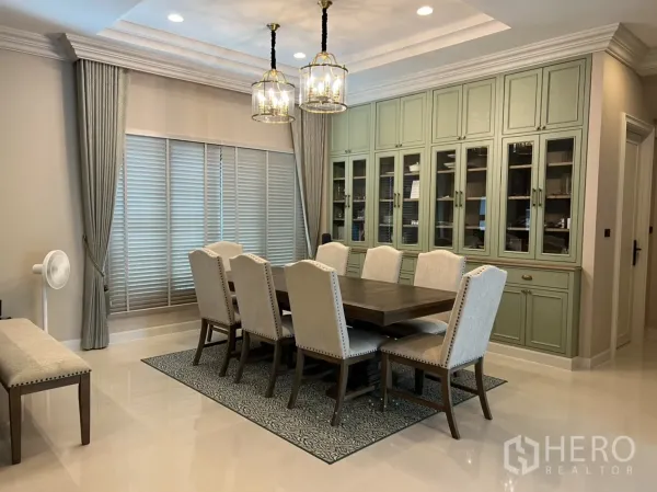 Detached House for rent or sale in Bang Kapi, Bangkok - Elegant dining room with an eight-seat table, pendant chandeliers and full-wall sage built-in cabinets with glass fronts.