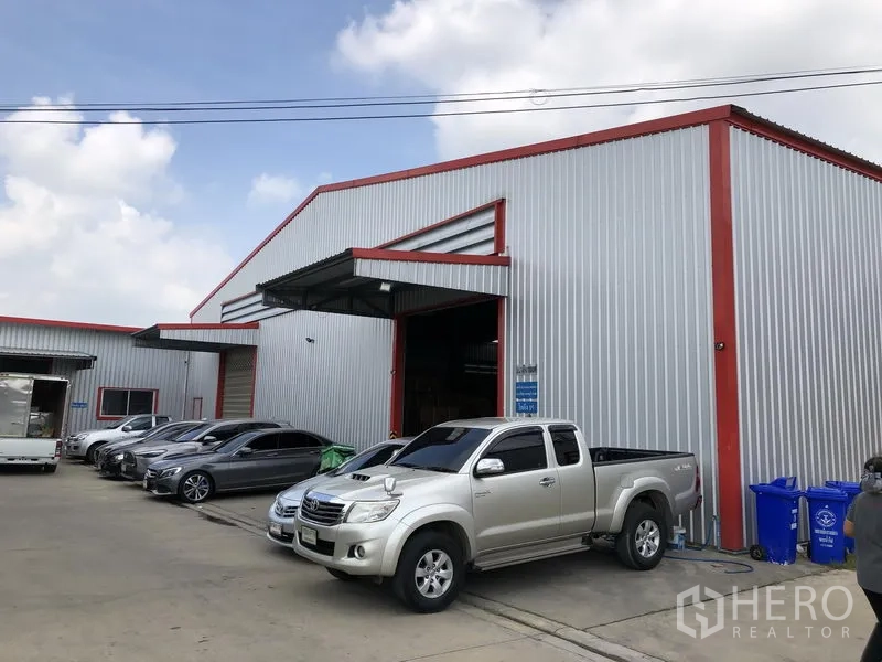 Warehouse for rent in Nonthaburi - Front exterior of a corrugated metal warehouse with red trim, open loading bay and car parking.