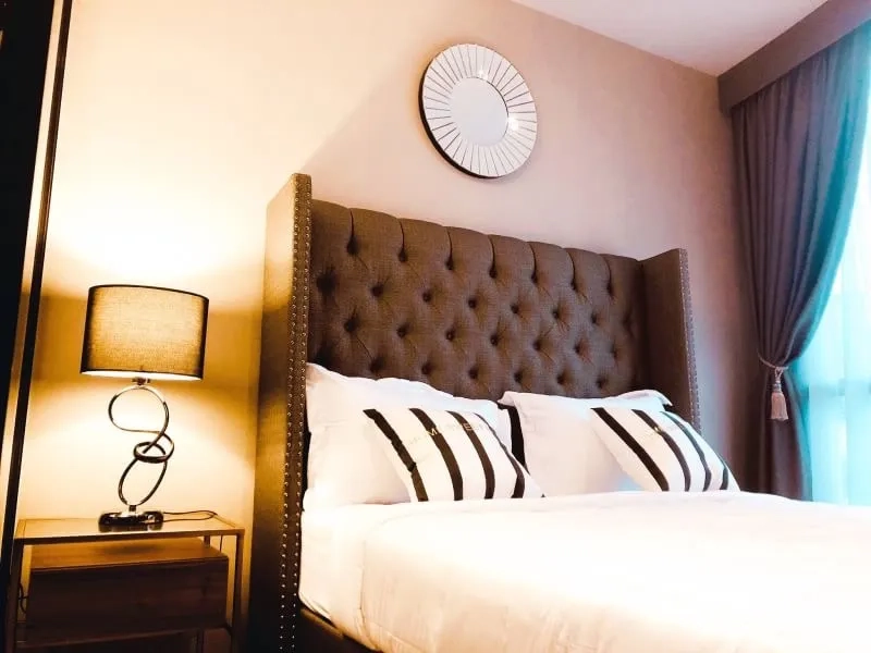 Condominium for rent in Watthana, Bangkok - Sunlit bedroom featuring a tufted headboard, bedside lamp and curtains.