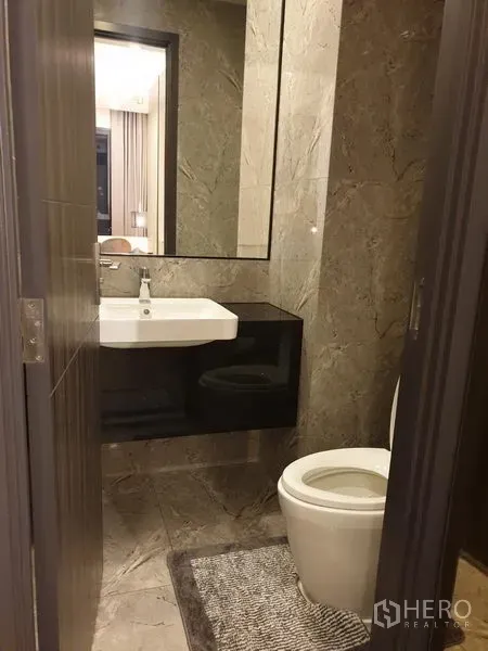 Condominium for rent in Watthana, Bangkok - Modern bathroom with marble tiles, large mirror, sink vanity and toilet.