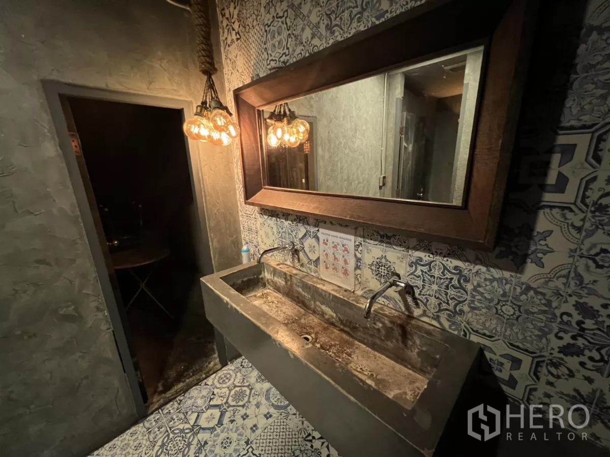 零售空间 出租 - 洗手区配长水泥台盆、大镜子与复古吊灯，花纹墙地砖。