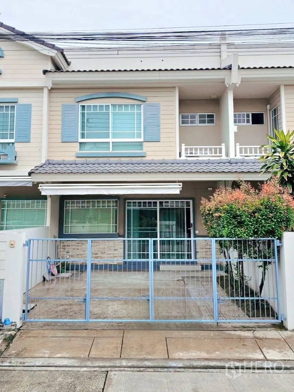 Townhouse for rent in Bang Phli, Samut Prakan - Front exterior with blue gate, paved patio for parking and sliding glass entrance.