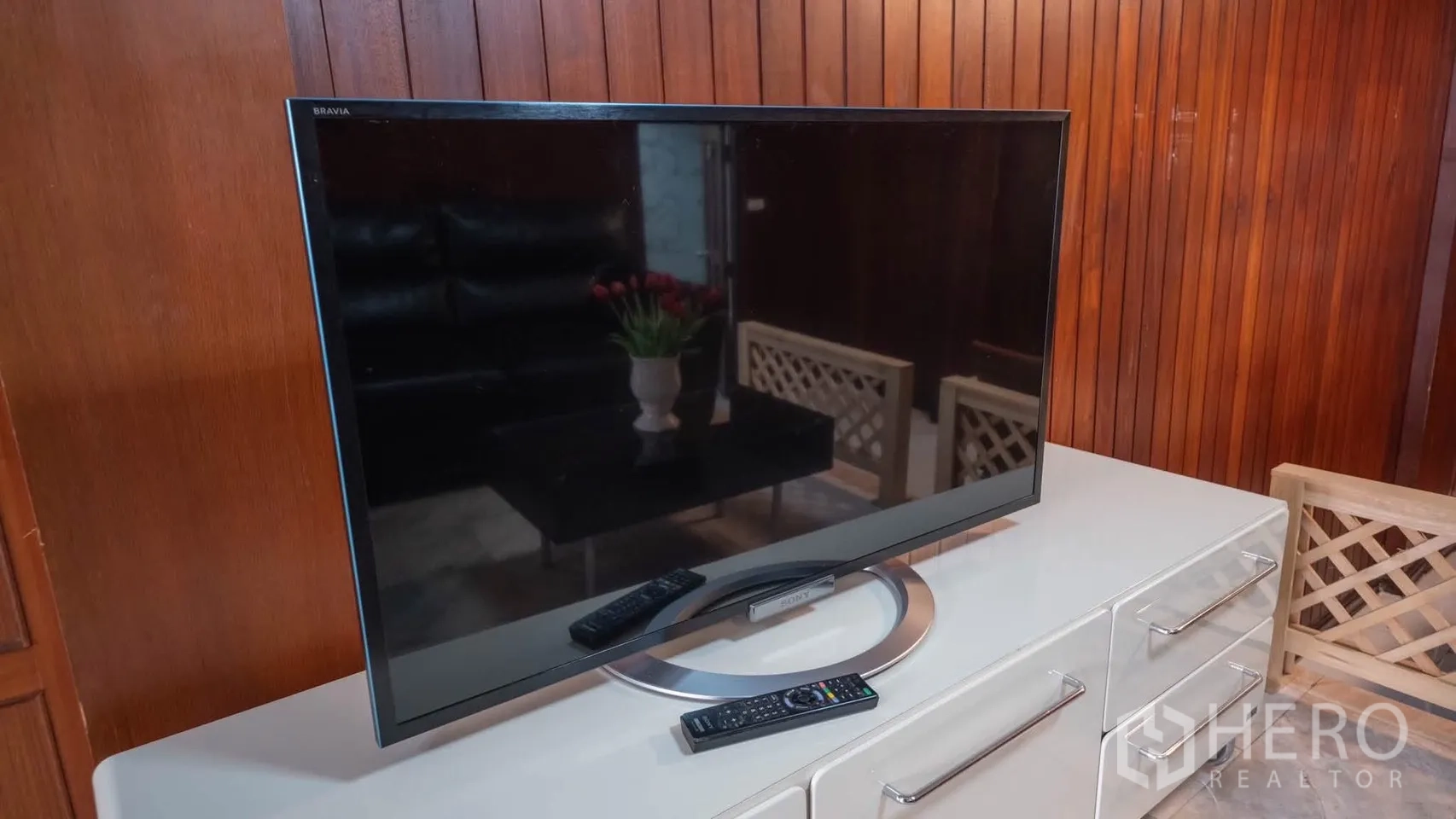 Townhouse for rent in Watthana, Bangkok - TV on a sleek white cabinet against a wood-paneled living room wall.