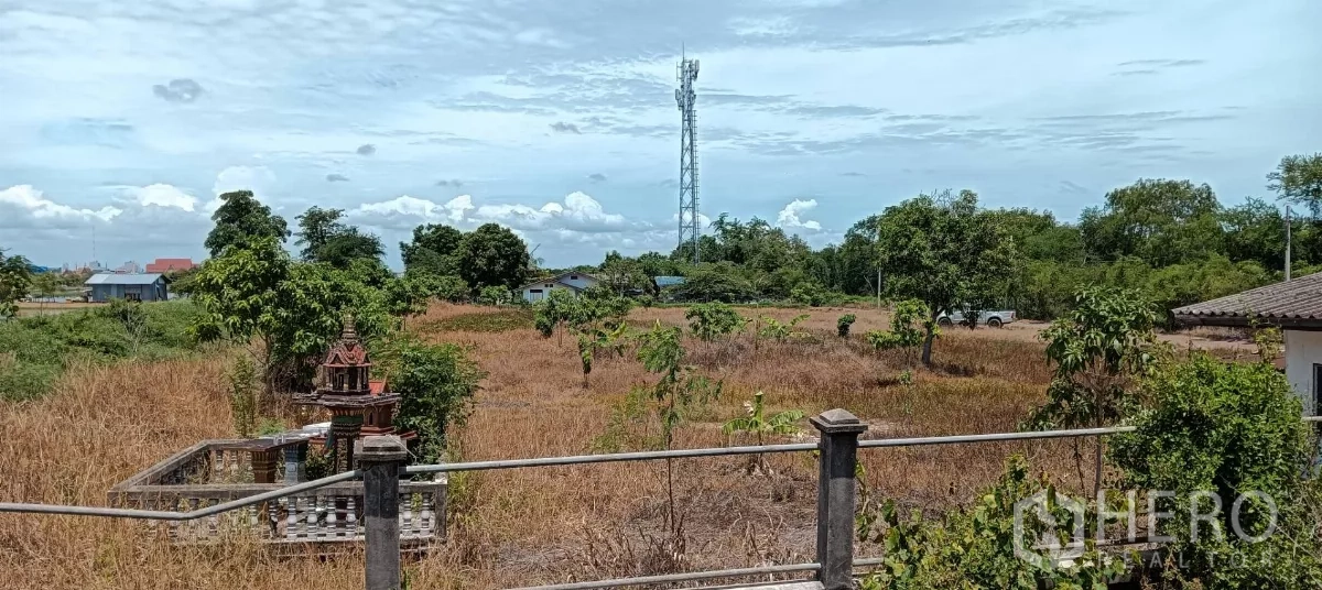 Land for sale in Bang Bo, Samut Prakan - Expansive land plot in Bang Bo with dry grass, trees, boundary fence and a telecom tower under a blue sky.