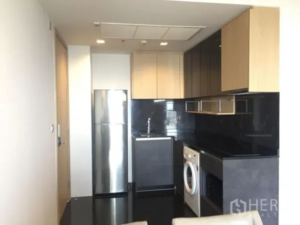Condominium for rent in Chatuchak, Bangkok - Modern compact kitchen with black stone backsplash, wood cabinets, stainless fridge and washing machine in a Chatuchak condo.