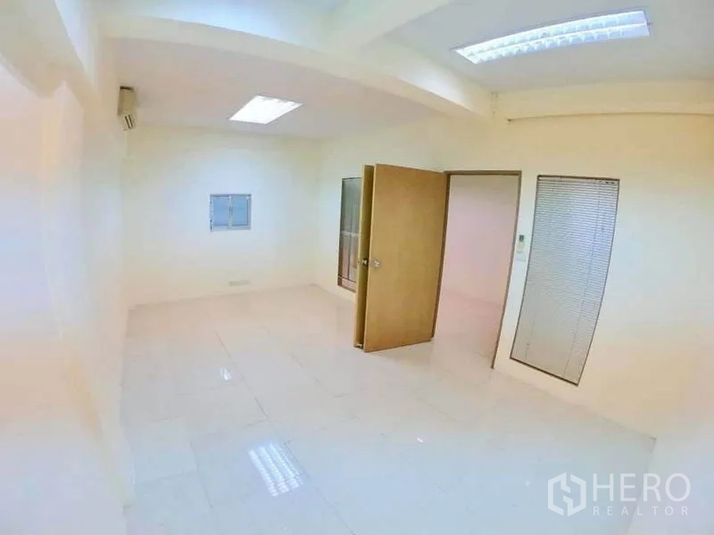 Office Space for rent in Khlong Toei, Bangkok - Clean white office room with tiled floor, internal windows and an open wooden door.