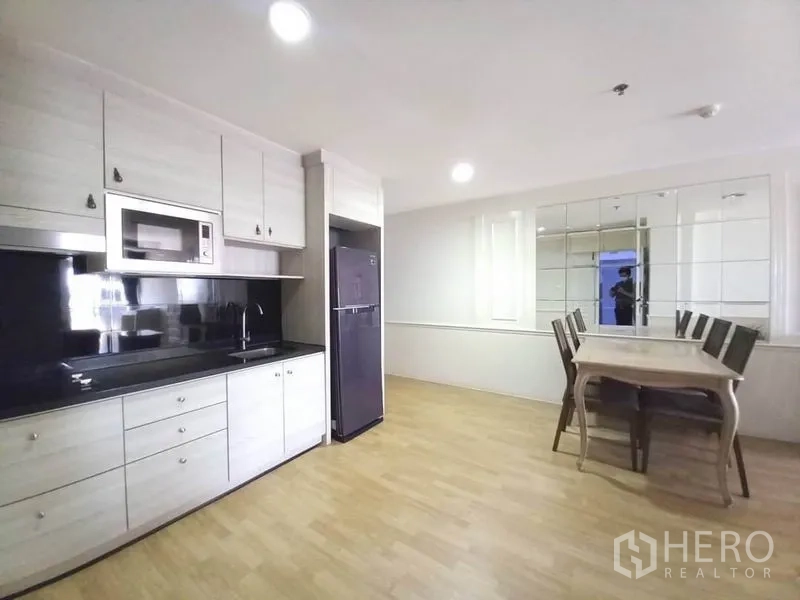 公寓 出租在Khlong Toei, Bangkok - 现代小厨房，黑色防溅板、微波炉、冰箱及餐桌。