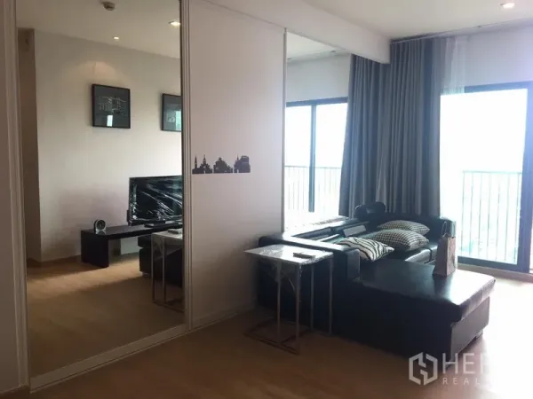 Condominium for rent in Khlong Toei, Bangkok - Open-plan lounge with L-shaped leather sofa, mirrored sliding door and two balcony doors bringing natural light.