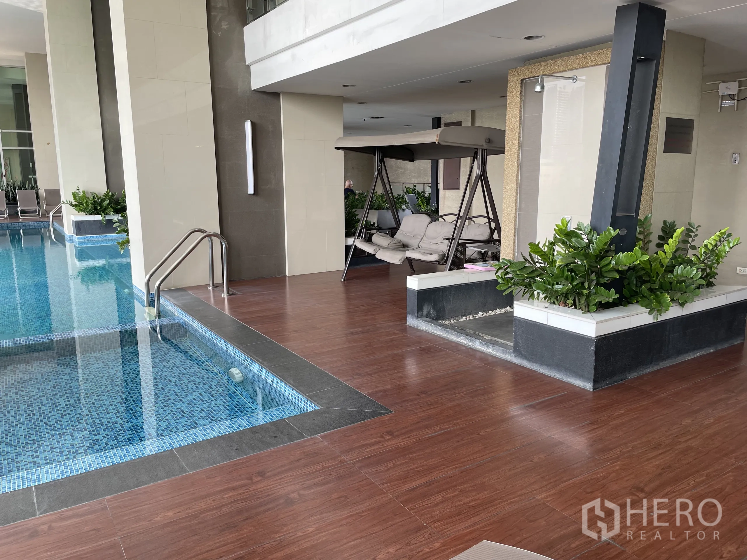 Condominium for sale in Chatuchak, Bangkok - Indoor pool deck with mosaic-tiled pool, shower area and cushioned swing seat.