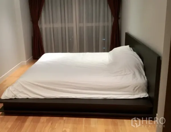 คอนโด ให้เช่าในKhlong Toei, Bangkok - ห้องนอนเงียบสงบ เตียงแพลตฟอร์ม พื้นไม้ และหน้าต่างสูงจรดเพดานพร้อมม่านสีเข้ม