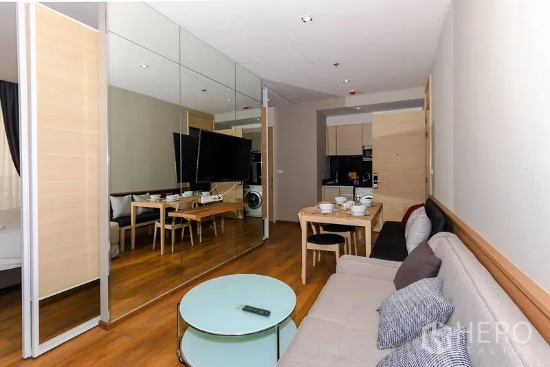 คอนโด ให้เช่าในKhlong Toei, Bangkok - ห้องนั่งเล่นแบบโอเพ่นพร้อมผนังกระจกเงา ทีวียึดผนัง ชุดโต๊ะทานอาหาร และพื้นไม้โทนอุ่น