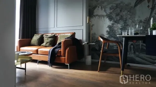 Condominium for rent in Watthana, Bangkok - Stylish living room with tan leather sofa, wood floors and a tropical mural feature wall.