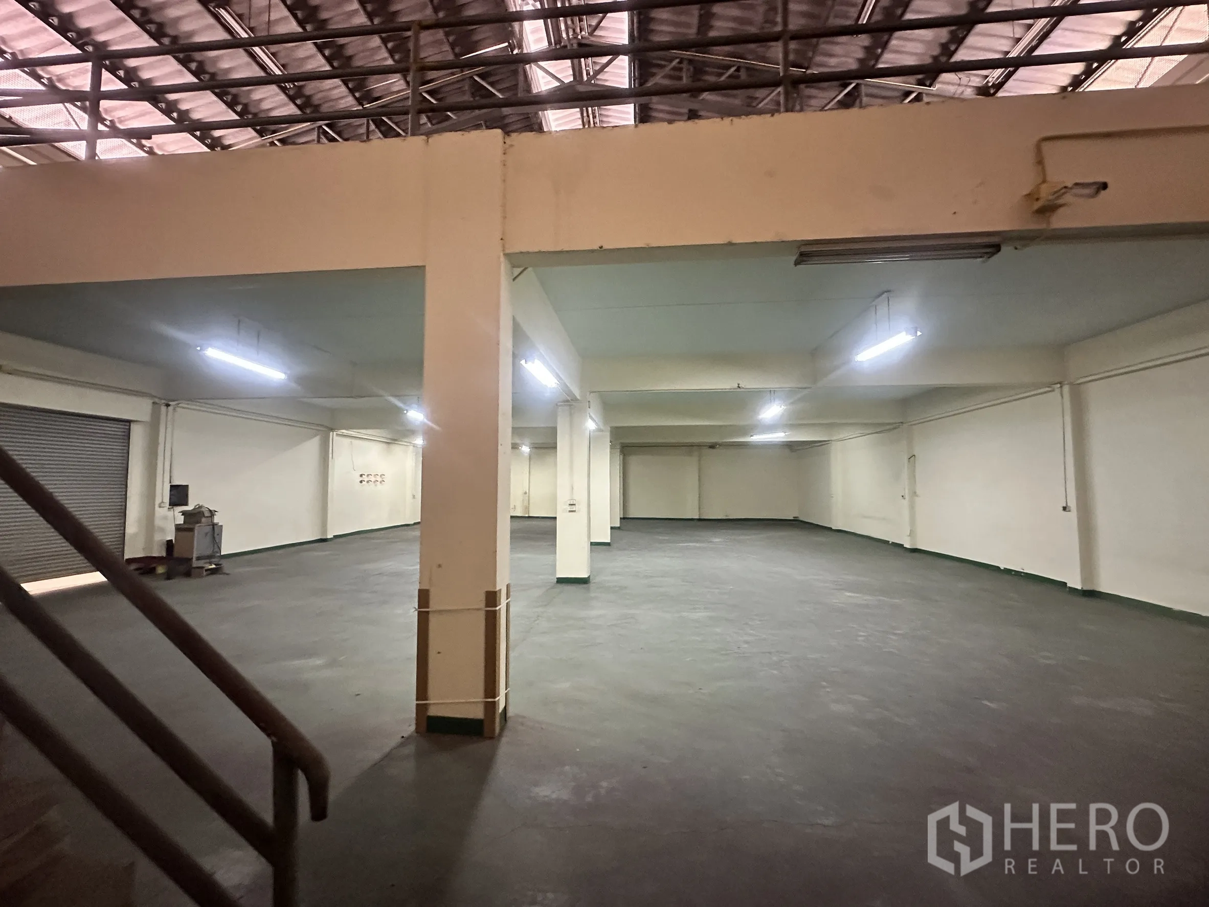 Factory for sale in Bang Bua Thong, Nonthaburi - Wide production space with columns, lit ceiling, and mezzanine edge.