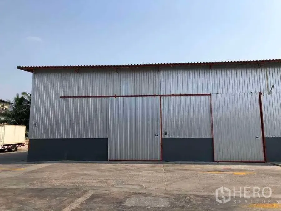 工厂 出租在Phra Pradaeng, Samut Prakan - 金属板外墙厂房外观，超大滑门与宽敞卡车通道，晴空下拍摄。