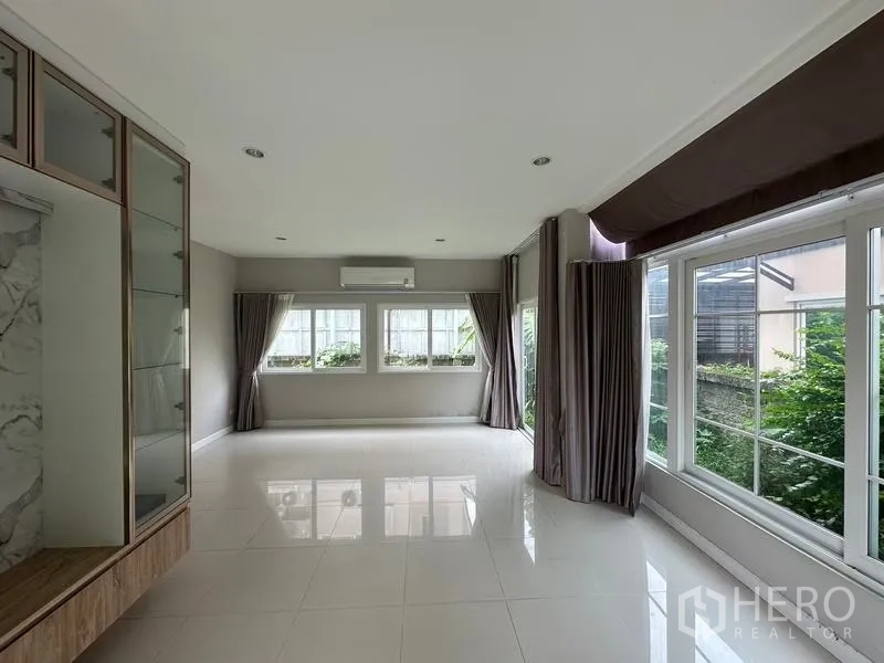 Detached House for sale in Bang Khen, Bangkok - Bright living room with white tile floors, large windows, and a built-in wall unit.
