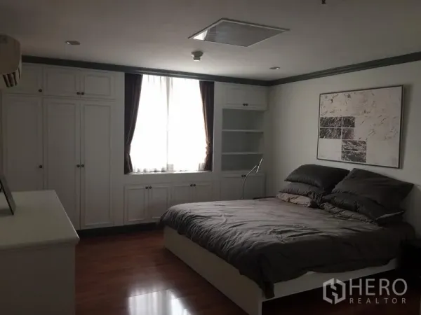 Condominium for rent in Watthana, Bangkok - Primary bedroom with double bed, large built-in wardrobes, wall art and a curtained window.