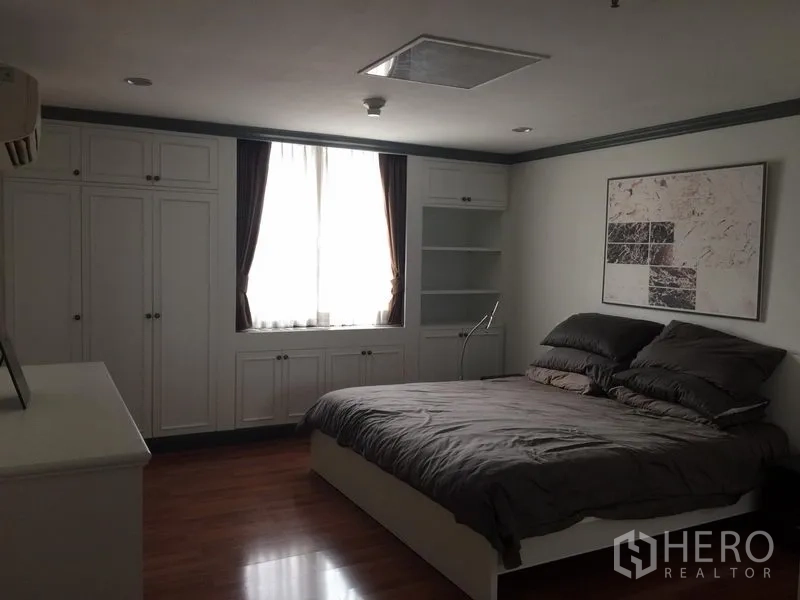 Condominium for rent in Watthana, Bangkok - Primary bedroom with double bed, large built-in wardrobes, wall art and a curtained window.